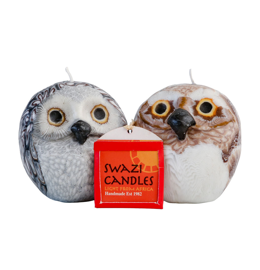 Two owl-shaped candles with a Swazi Candles sign between them on a white background