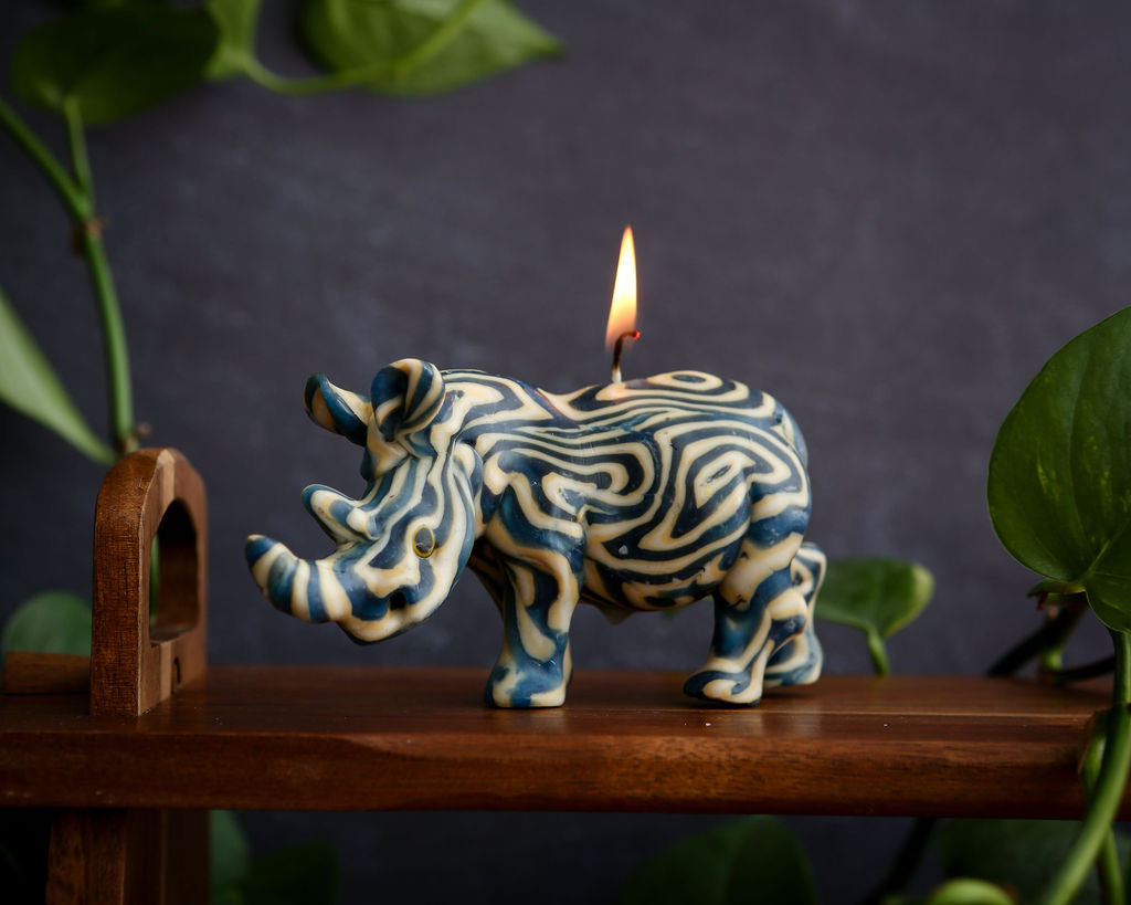 Rhino candle with a lit wick on a wooden surface with a dark background and plants.