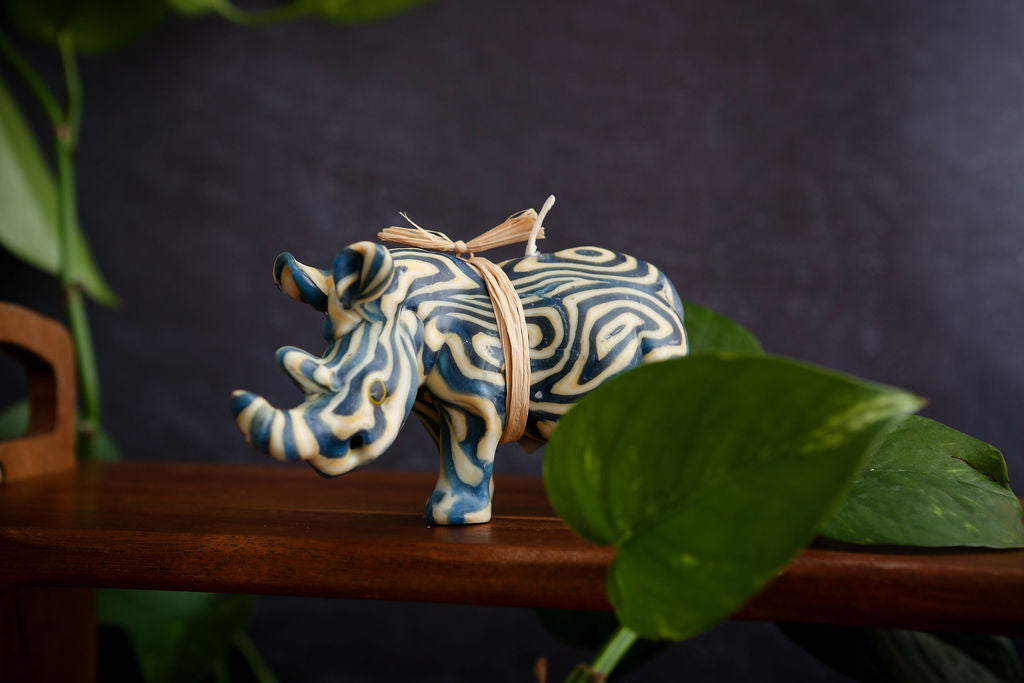 Decorative rhinoceros candle with blue and white patterns on a wooden surface with leaves in the background.