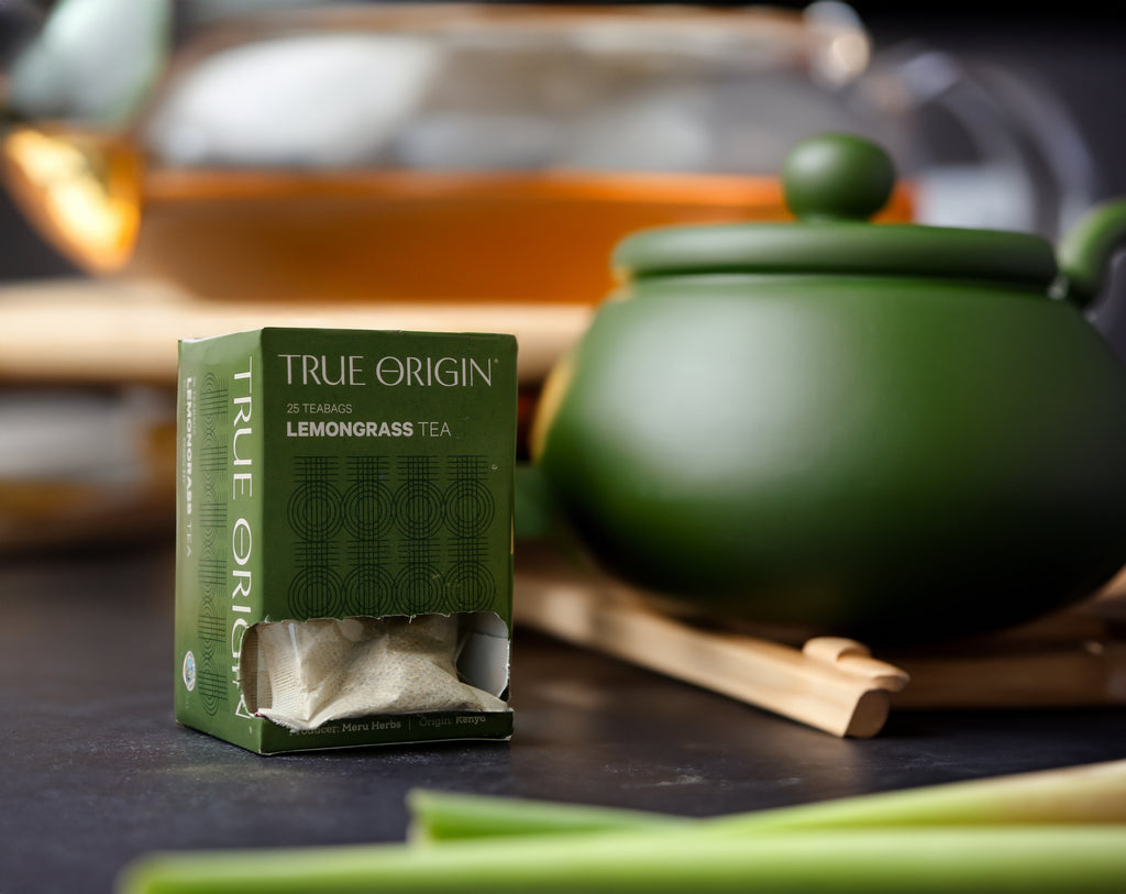 An opened box of True Origin Lemongrass Tea with 25 tea bags, produced by Meru Herbs, origin Kenya.  It is sitting next to a green teapot.