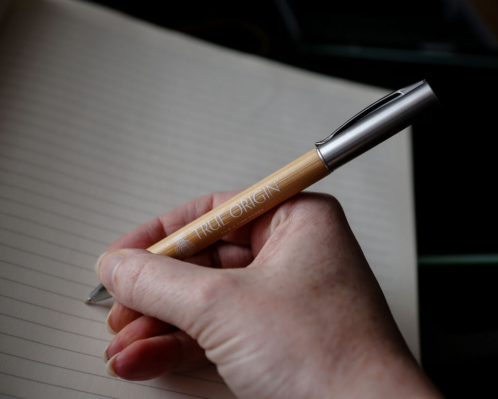 A bamboo and silver pen with a white True Origin logo and symbol.