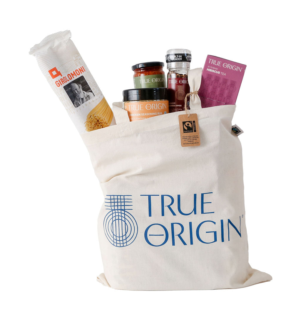 A cream Fairtrade cotton tote bag with the blue stacked True Origin logo with some True Origin products sticking out the top.
